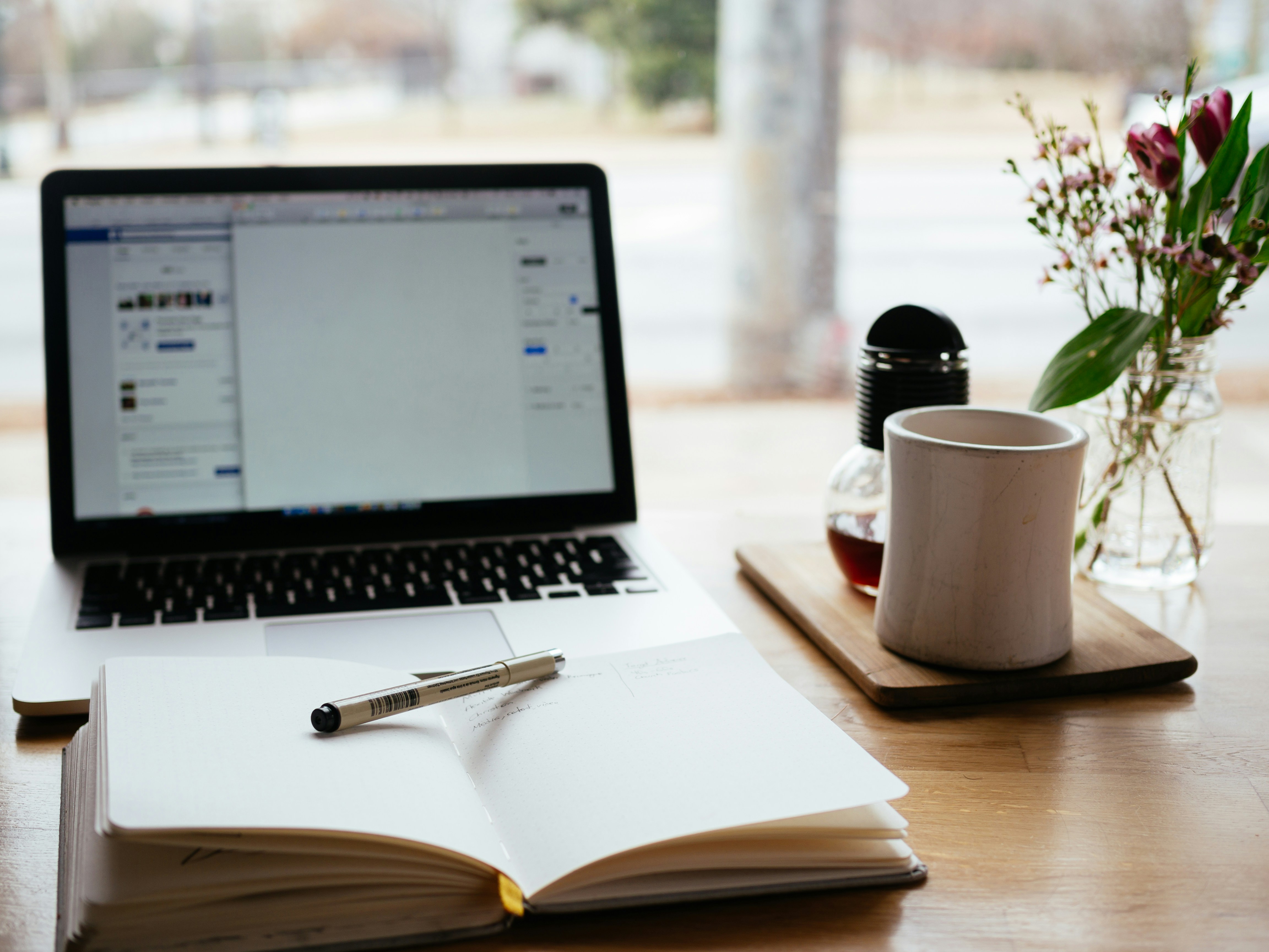 Laptop, open notebook, and coffee on a sunlit desk